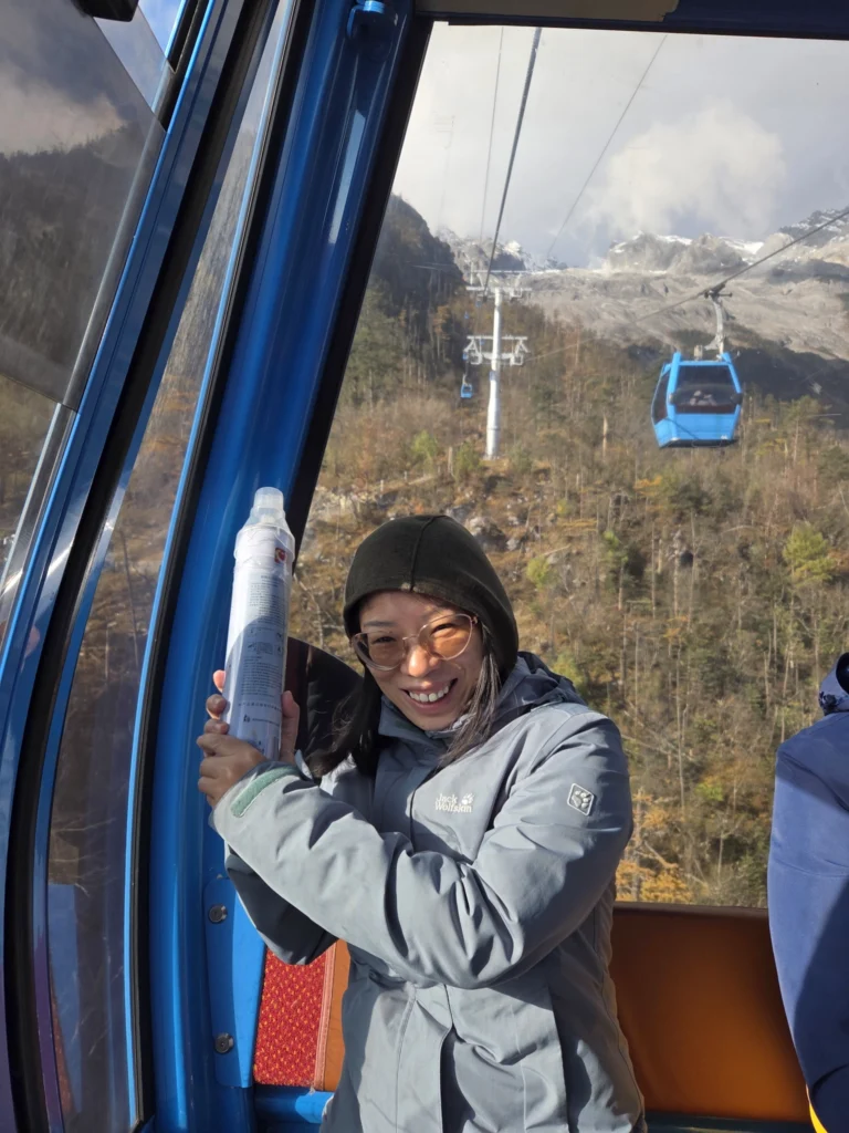 Rong in der Gondel der Seilbahn, Sie hält eine Sauerstoffflasche in der Hand