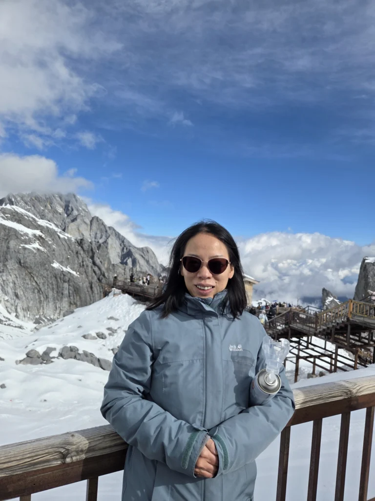 Rong mit Berge und Wolken im Hintergrund, ergänzend sind die Treppenanlage und Stege die dem Berg hinaufführen zu sehen.