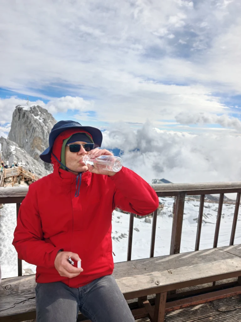 Stefan mit Gebirge im Hintergrund, er stärkt sich mit Wasser