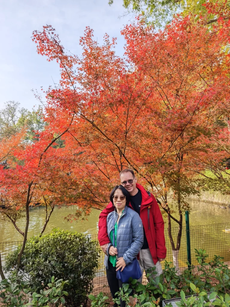 Rong und Stefan vor einem Baum mit rötlichen Blättern